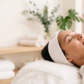 Person relaxing in a spa, eyes closed, with a white headband on and a towel-covered table.